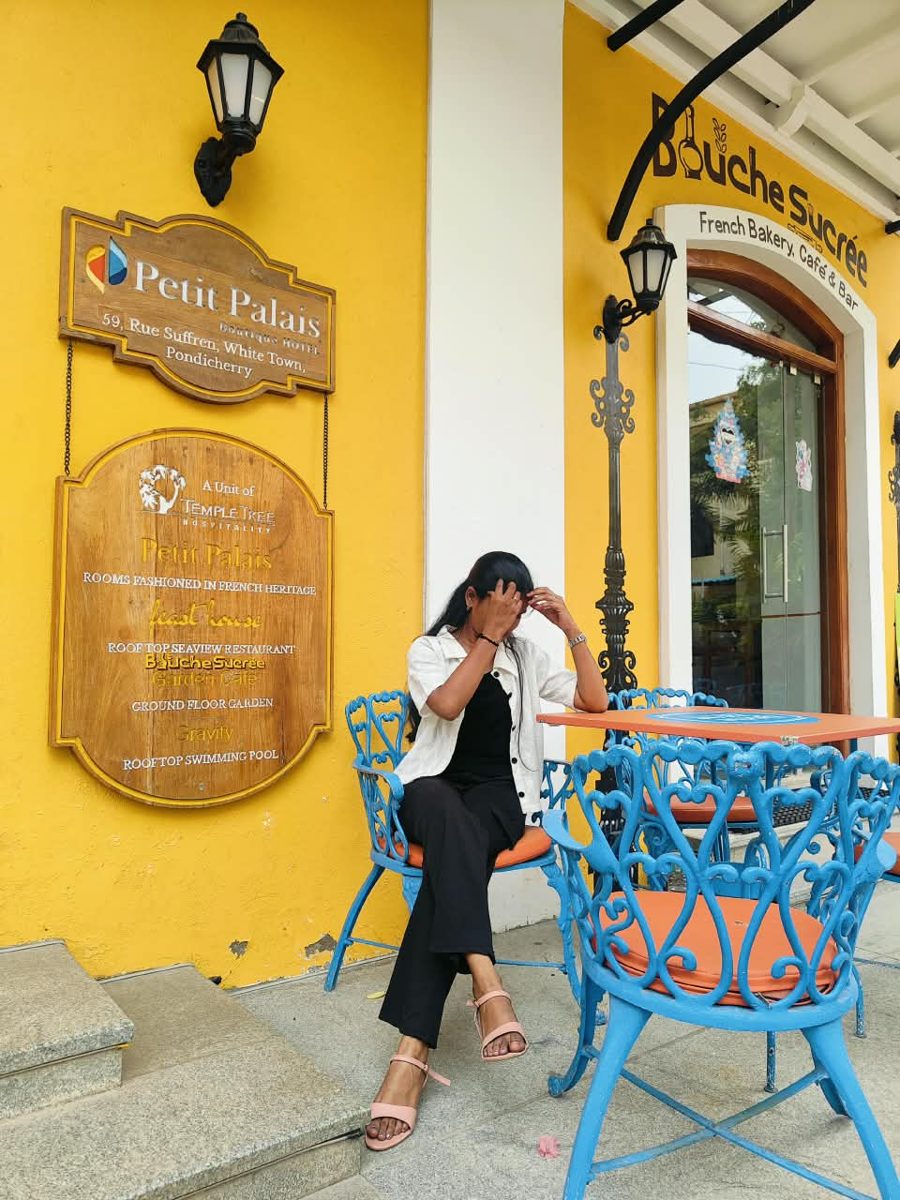 Bhargavi sitting at a blue cafe table against a bright yellow wall in Pondicherry